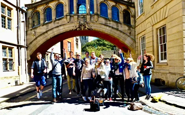 A corporate group receiving a private walking tour of Oxford. They are passing through the Bridge of Sighs in the sunlight.