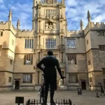 A statue in front of a big building in Oxford that can be seen from one of the private walking Tours of Oxford with Chris Peters. The sun is shining on the building and the statue stands in the shade in this image.