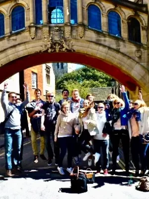 A corporate group receiving a private walking tour of Oxford. They are passing through the Bridge of Sighs in the sunlight.